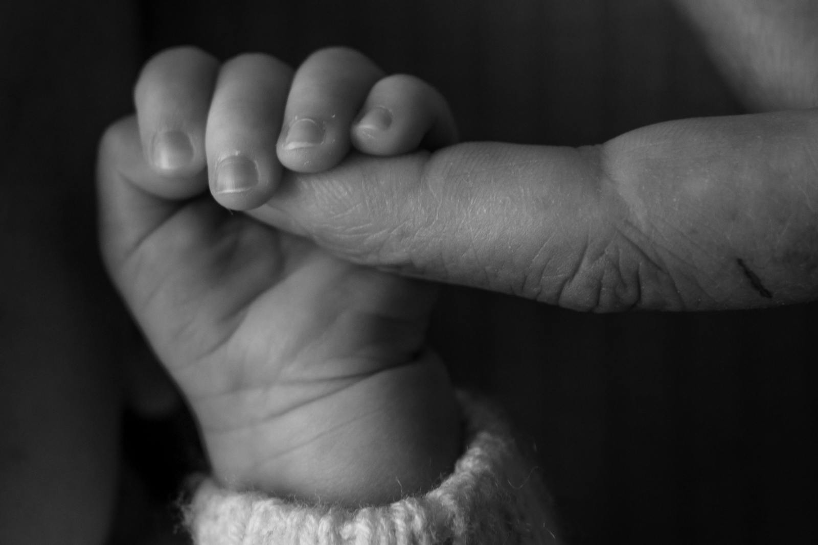 Maličké dětské prsty se drží dokořenu prstu dospělého