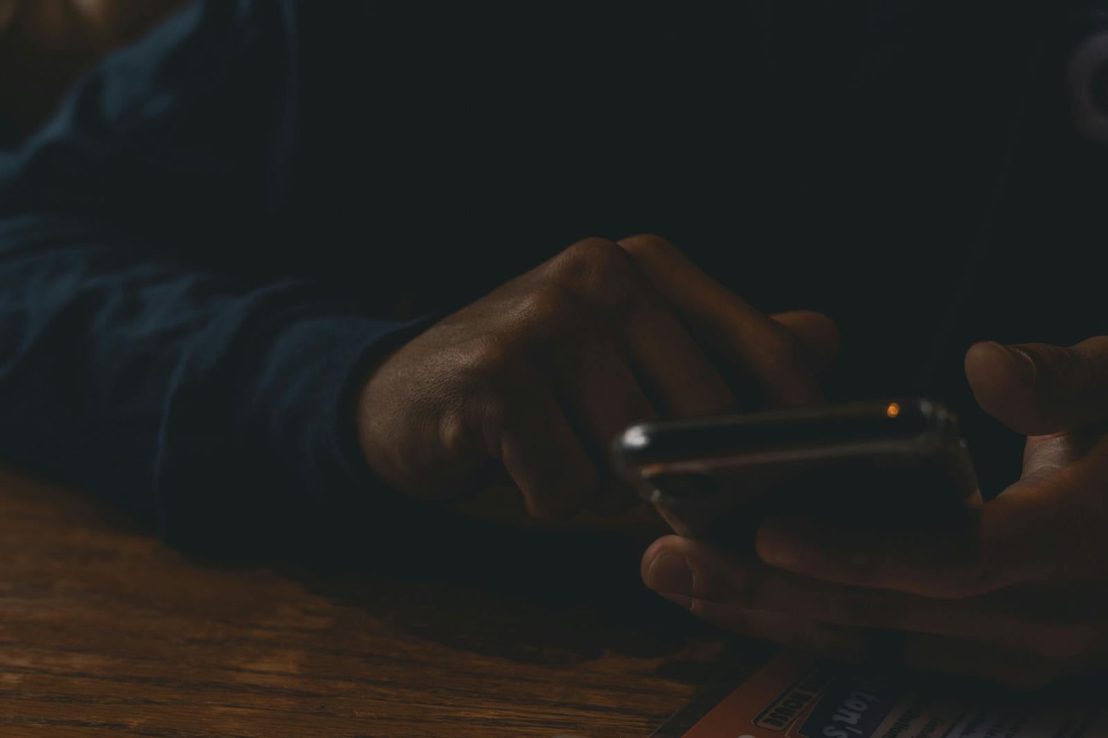 Detail rukou držících telefon v přítmí